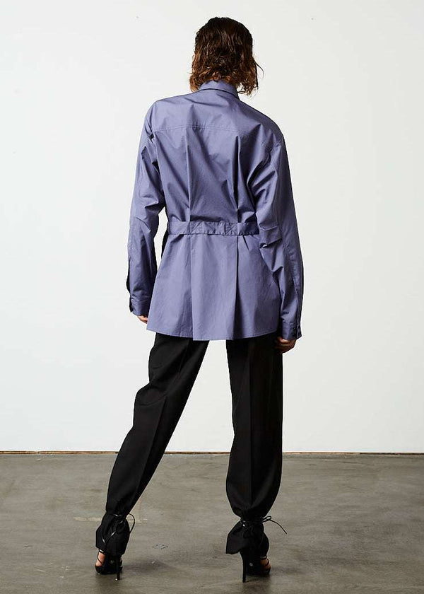 INTERNATIONAL CITIZEN.  Style: Artist Shirt. Back full body view. Style has an oversized shirt with a pen pocket at the chest, open underarms for breathability, and back belt ties that adjust at the front with silver rings. The shirt are made of Italian organic Cotton in Dreamstate Purple. Spiritually Infused, Sustainable Luxury Fashion in Berlin.
