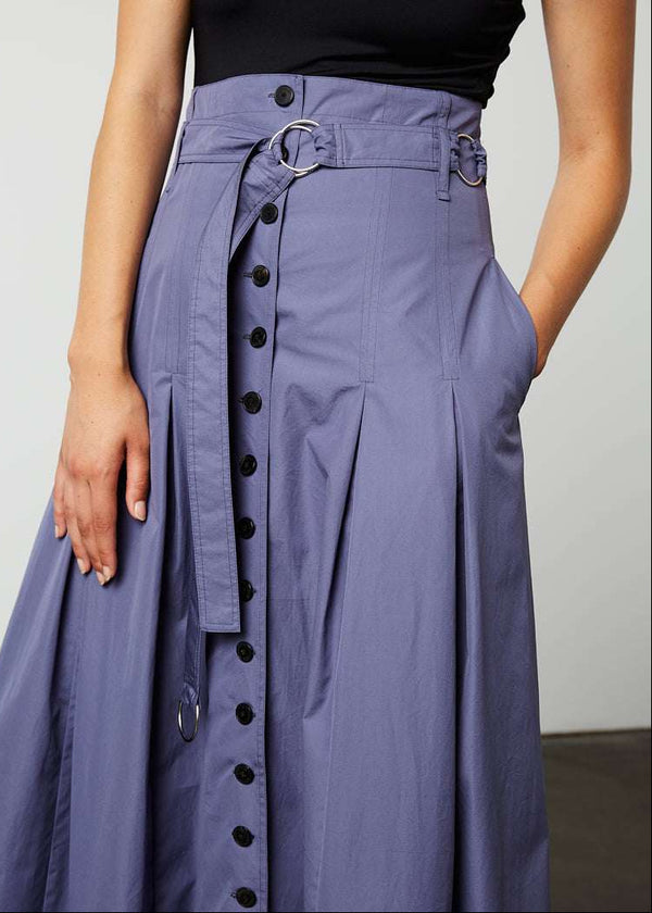 INTERNATIONAL CITIZEN.  Style: Button Skirt. Close up front view. A Button Skirt with box pleats below the hips. Detachable belt with silver ring details for closure. The skirt is made of Italian organic Cotton in Dreamstate Purple. Spiritually Infused, Sustainable Luxury Fashion in Berlin.