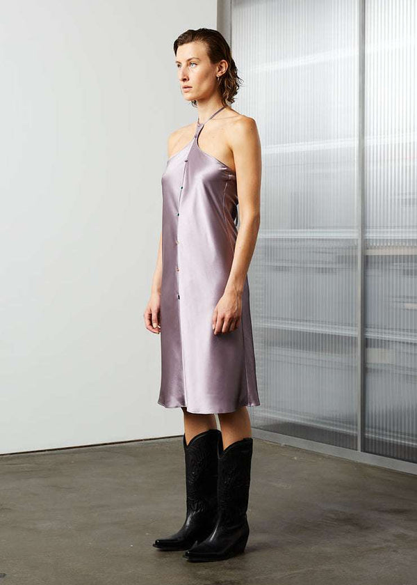 INTERNATIONAL CITIZEN.  Style: The Short Chakra Slip Dress is cut on the bias and features hand sewn crystals down the front to represent the 7-Chakras. The neckline has long straps that tie at the back neck. Made of Organic Silk, Fluorite Purple. Spiritually Infused, Sustainable Luxury Fashion in Berlin. Side front photo.
