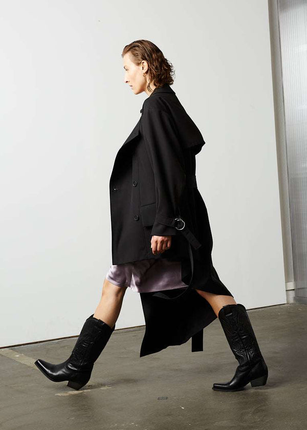 INTERNATIONAL CITIZEN.  Style: The Eclipse Jacket. A unisex, asymmetrical along the hemline and oversized with soft shoulder pads for collapsed structure.Side walking view.  Made of Italian RWS Wool, Obsidian Black. Spiritually Infused, Sustainable Luxury Fashion in Berlin.