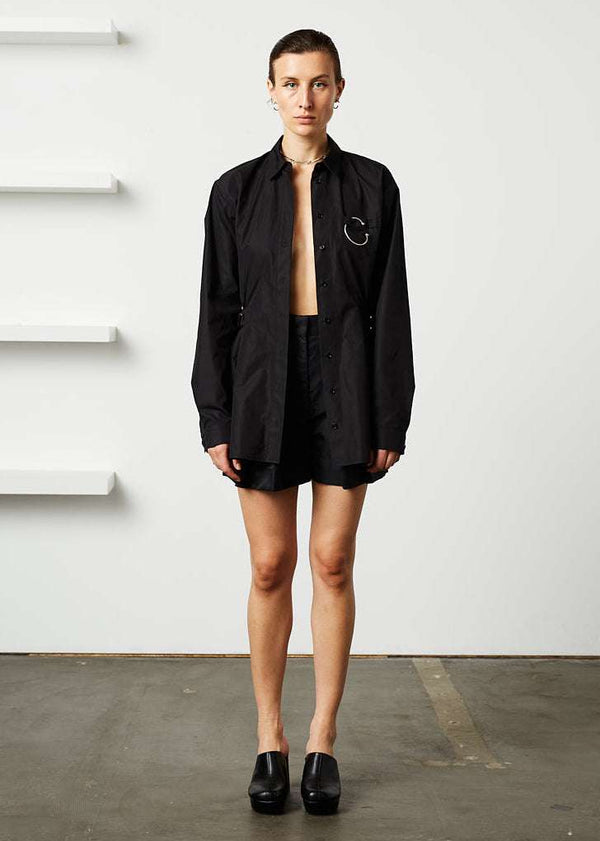 INTERNATIONAL CITIZEN.  Style: Artist Shirt. Photo shown un-buttoned. Style has an oversized shirt with a pen pocket at the chest, open underarms for breathability, and back belt ties that adjust at the front with silver rings. The shirt is made of Italian organic Cotton in Obsidian Black. Spiritually Infused, Sustainable Luxury Fashion in Berlin.