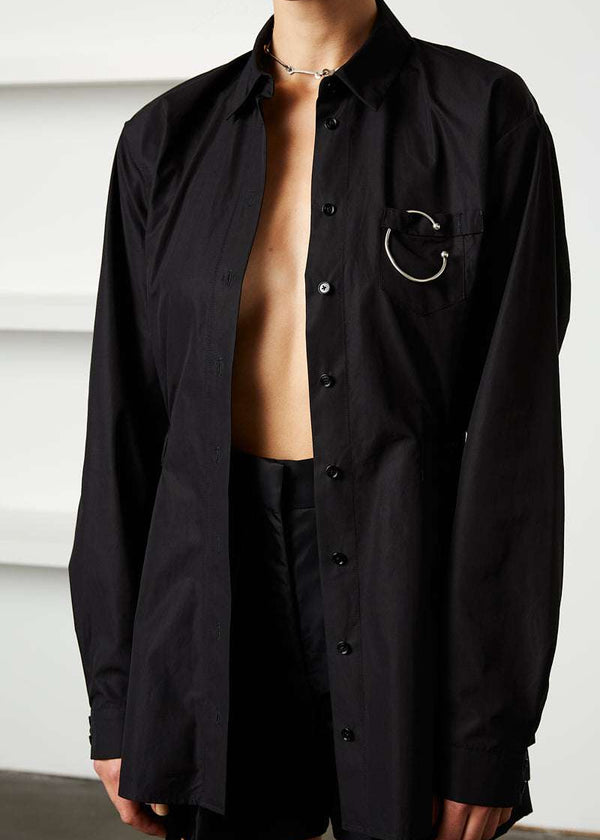 INTERNATIONAL CITIZEN.  Style: Artist Shirt. Close up photo un-buttoned. Style has an oversized shirt with a pen pocket at the chest, open underarms for breathability, and back belt ties that adjust at the front with silver rings. The shirt is made of Italian organic Cotton in Obsidian Black. Spiritually Infused, Sustainable Luxury Fashion in Berlin.
