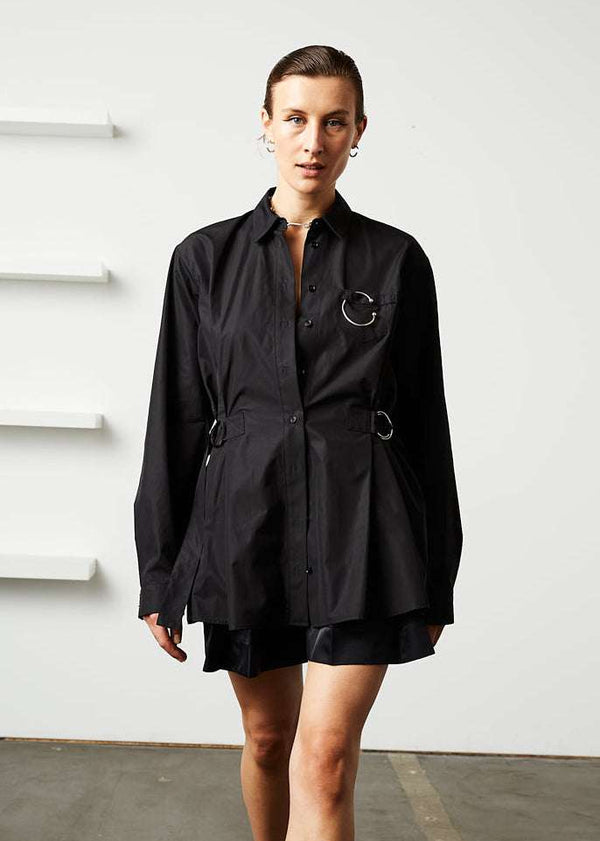 INTERNATIONAL CITIZEN.  Style: Artist Shirt. Front photo buttoned up. Style has an oversized shirt with a pen pocket at the chest, open underarms for breathability, and back belt ties that adjust at the front with silver rings. The shirt is made of Italian organic Cotton in Obsidian Black. Spiritually Infused, Sustainable Luxury Fashion in Berlin.