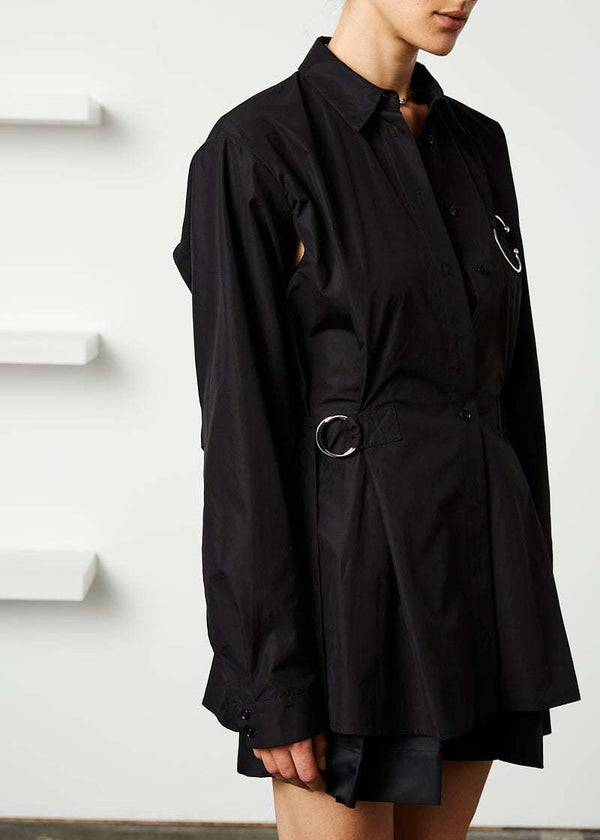 INTERNATIONAL CITIZEN.  Style: Artist Shirt. Side view. Style has an oversized shirt with a pen pocket at the chest, open underarms for breathability, and back belt ties that adjust at the front with silver rings. The shirt is made of Italian organic Cotton in Obsidian Black. Spiritually Infused, Sustainable Luxury Fashion in Berlin.
