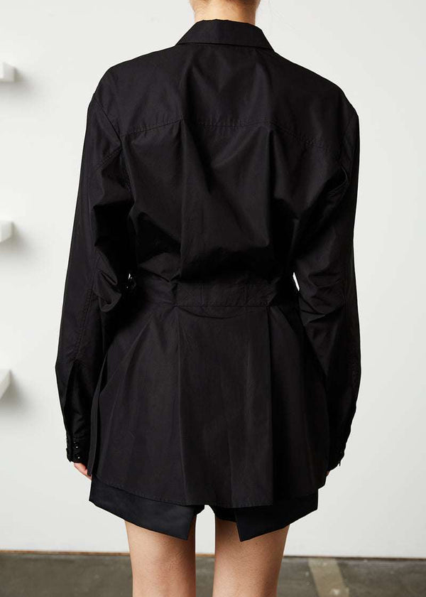 INTERNATIONAL CITIZEN.  Style: Artist Shirt. Back photo. Style has an oversized shirt with a pen pocket at the chest, open underarms for breathability, and back belt ties that adjust at the front with silver rings. The shirt is made of Italian organic Cotton in Obsidian Black. Spiritually Infused, Sustainable Luxury Fashion in Berlin.

