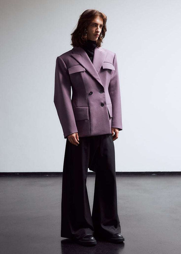 INTERNATIONAL CITIZEN.  Style: The Hourglass Jacket is named after its perfected silhouette, shaped with a nipped waist. It is double breasted with a 3-button closures and classic men’s tailoring techniques within the structure of the body. It has welt flap pockets and oversized bent sleeve. Unisex Item. Worn by male model in this photo. Made of Italian Wool, certified RWS, Amethyst Purple. Spiritually Infused, Sustainable Luxury Fashion in Berlin.