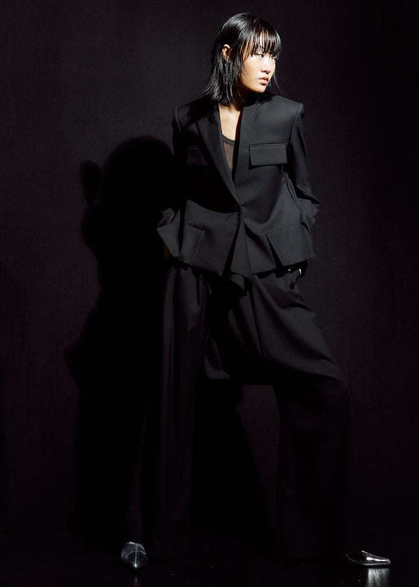 INTERNATIONAL CITIZEN.  Style: The Ascension Jacket. Front view. Style has a tailored structured front body, bias under sleeves for a slim fit, an asymmetrical cascading back body on the bias, an asymmetrical collar and lapel. Lastly it has a handkerchief detail at the front button closure. The jacket is made of Italian RWS Wool in Obsidian Black. Spiritually Infused, Sustainable Luxury Fashion in Berlin.