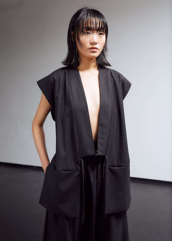 INTERNATIONAL CITIZEN.  Style: The Kimono Vest has a longer front body with inseam pockets and short back body. Unisex Item. Worn open. Made of Italian Wool, certified (RWS) Responsible Wool Standard, Obsidian Black. Spiritually Infused, Sustainable Luxury Fashion in Berlin.