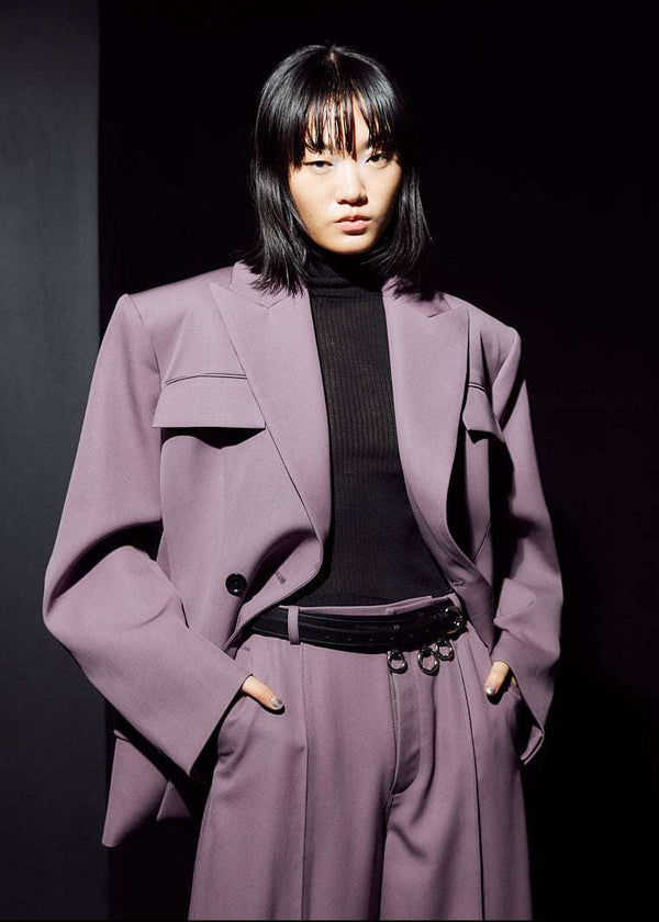 INTERNATIONAL CITIZEN.  Style: The Hourglass Jacket is named after its perfected silhouette, shaped with a nipped waist. It is double breasted with a 3-button closures, felt under collar and classic men’s tailoring techniques within the structure of the body. Close up front photo worn open. Unisex Item. Made of Italian Wool, certified RWS, Amethyst Purple. Spiritually Infused, Sustainable Luxury Fashion in Berlin.