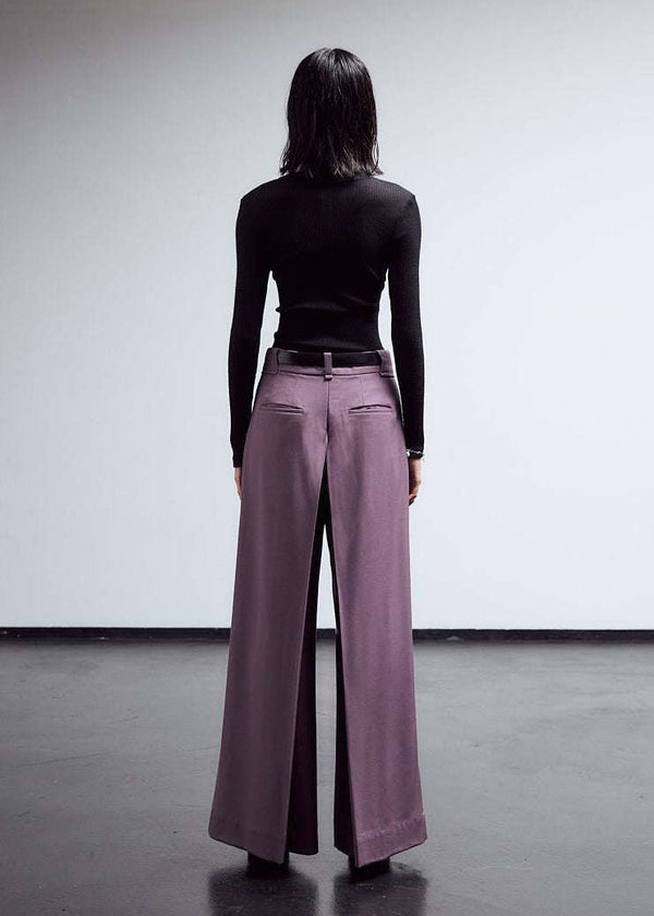 INTERNATIONAL CITIZEN.  Style: The Deep Pleated Pant, falls below the natural waist. The pleats nearly meet at the center back. Made of Italian RWS Wool, Amethyst Purple. Full body back view. Spiritually Infused, Sustainable Luxury Fashion in Berlin.