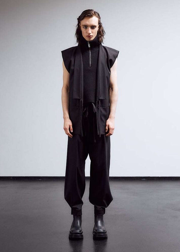 INTERNATIONAL CITIZEN.  Style: The JiuJitsu Pants are have a drawstring closer at the waist,  a straight leg with silver snap hem straps and a thigh patch. Unisex item. Full front male model photo. Made of Italian Wool, certified (RWS) Responsible Wool Standard, Obsidian Black. Spiritually Infused, Sustainable Luxury Fashion in Berlin.
