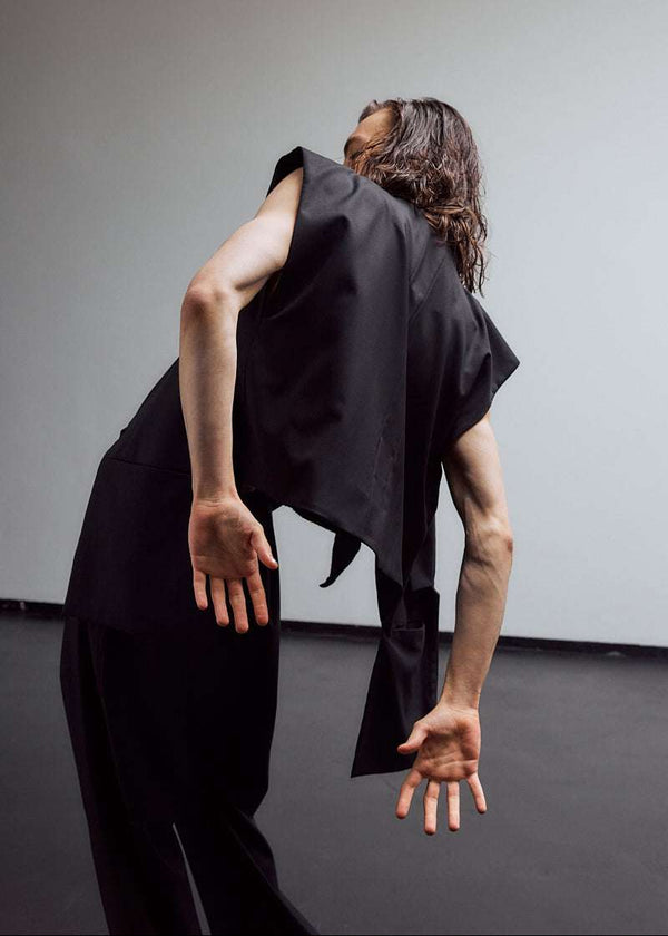 INTERNATIONAL CITIZEN.  Style: The Kimono Vest has a longer front body with inseam pockets and short back body. Unisex Item. Male back body photo. Made of Italian Wool, certified (RWS) Responsible Wool Standard, Obsidian Black. Spiritually Infused, Sustainable Luxury Fashion in Berlin.