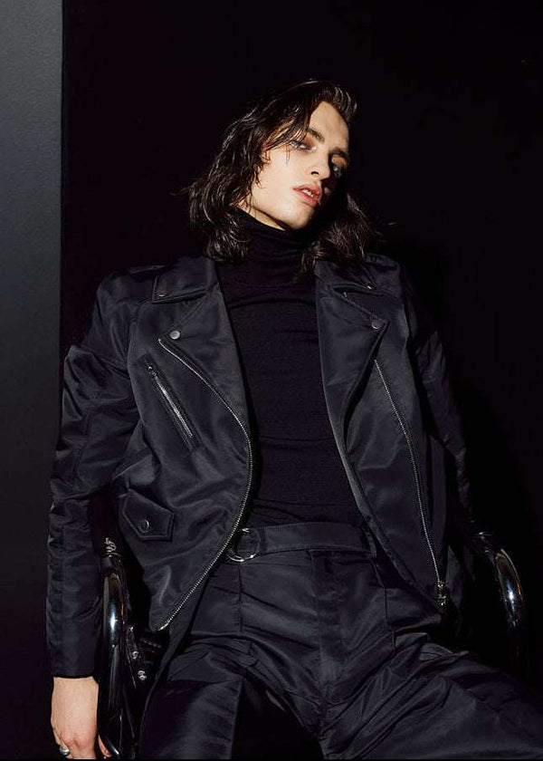 INTERNATIONAL CITIZEN.  Style: The M23 Moto Jacket has classic moto detailing and an innovative drape at the back shoulder creating a soft strength in the silhouette. Unisex Item. Male front photo. Made of Italian post-consumer recycled Nylon, Obsidian Black. Spiritually Infused, Sustainable Luxury Fashion in Berlin.