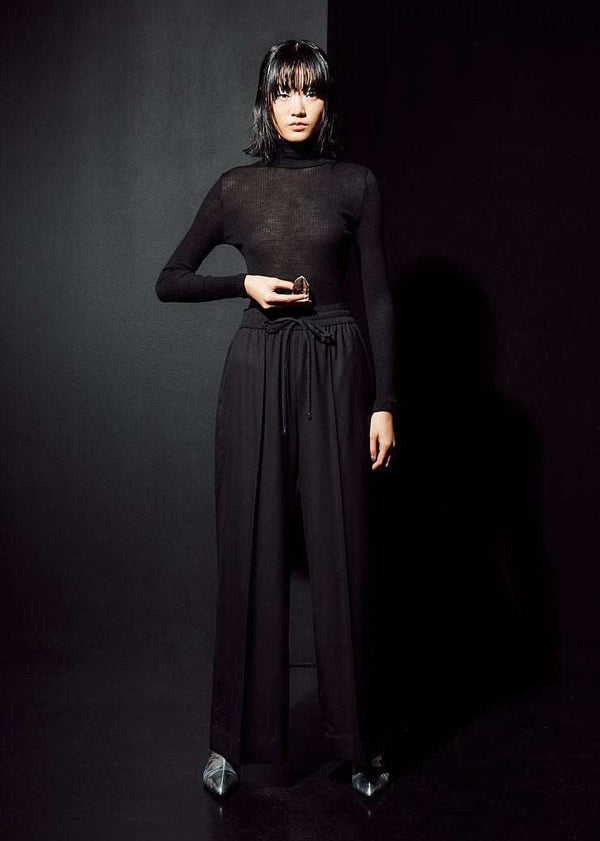 INTERNATIONAL CITIZEN.  Style: The Arcana Pant. Front full body photo. Style has a relaxed fit with front pin-tucks and excessive volume eased into the waistband. Unisex Item. The pants are made of Italian RWS Wool in Obsidian Black. Spiritually Infused, Sustainable Luxury Fashion in Berlin.