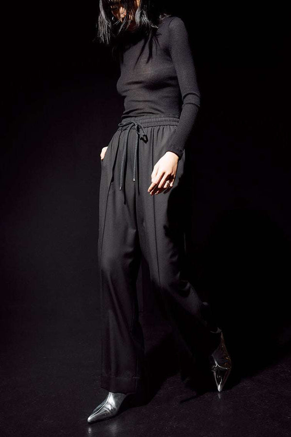INTERNATIONAL CITIZEN.  Style: The Arcana Pant. Front movement photo. Style has a relaxed fit with front pin-tucks and excessive volume eased into the waistband. Unisex Item. The pants are made of Italian RWS Wool in Obsidian Black. Spiritually Infused, Sustainable Luxury Fashion in Berlin.