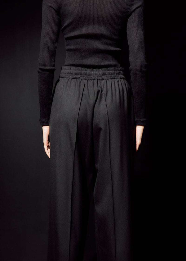 INTERNATIONAL CITIZEN.  Style: The Arcana Pant. Close up back body photo. Style has a relaxed fit with front pin-tucks and elastic waistband. Unisex Item. The pants are made of Italian RWS Wool in Obsidian Black. Spiritually Infused, Sustainable Luxury Fashion in Berlin.