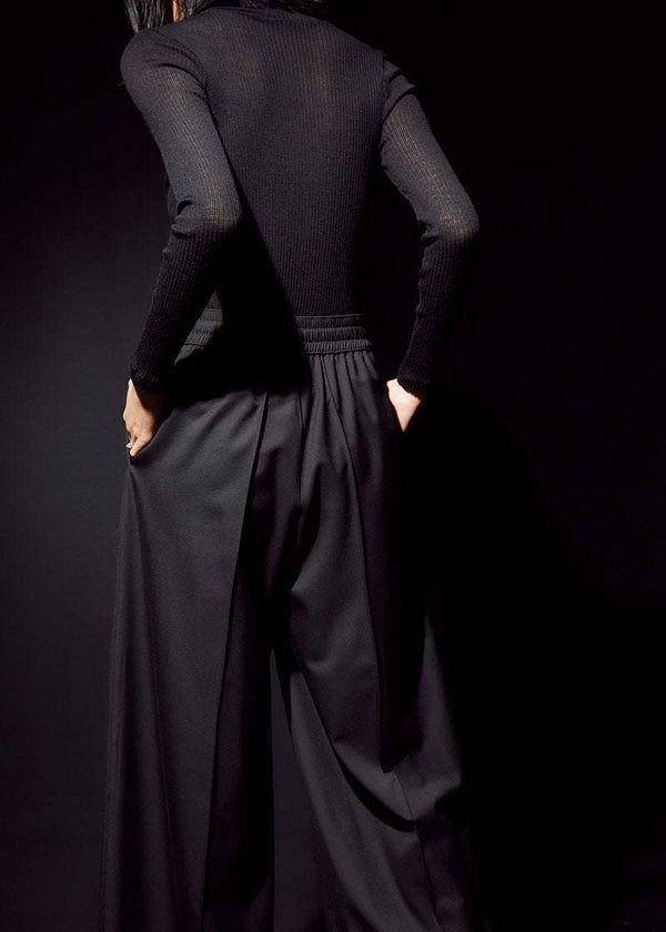 INTERNATIONAL CITIZEN.  Style: The Arcana Pant. Close up back view. Style has a relaxed fit with front pin-tucks and excessive volume eased into the waistband. Unisex Item. The pants are made of Italian RWS Wool in Obsidian Black. Spiritually Infused, Sustainable Luxury Fashion in Berlin.