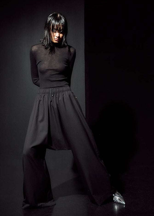 INTERNATIONAL CITIZEN.  Style: The Lanna Pant have a dropped crotch with excessive volume eased into an elastic waistband, drawcord and inseam pockets. Unisex Item. Full body front photo. Made of Italian Wool, certified (RWS) Responsible Wool Standard, Obsidian Black. Spiritually Infused, Sustainable Luxury Fashion in Berlin.
