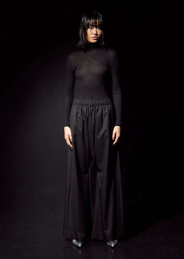 INTERNATIONAL CITIZEN.  Style: The Lanna Pant have a dropped crotch with excessive volume eased into an elastic waistband. Unisex Item. Female front photo. Made of Italian Wool, certified (RWS) Responsible Wool Standard, Obsidian Black. Spiritually Infused, Sustainable Luxury Fashion in Berlin.
