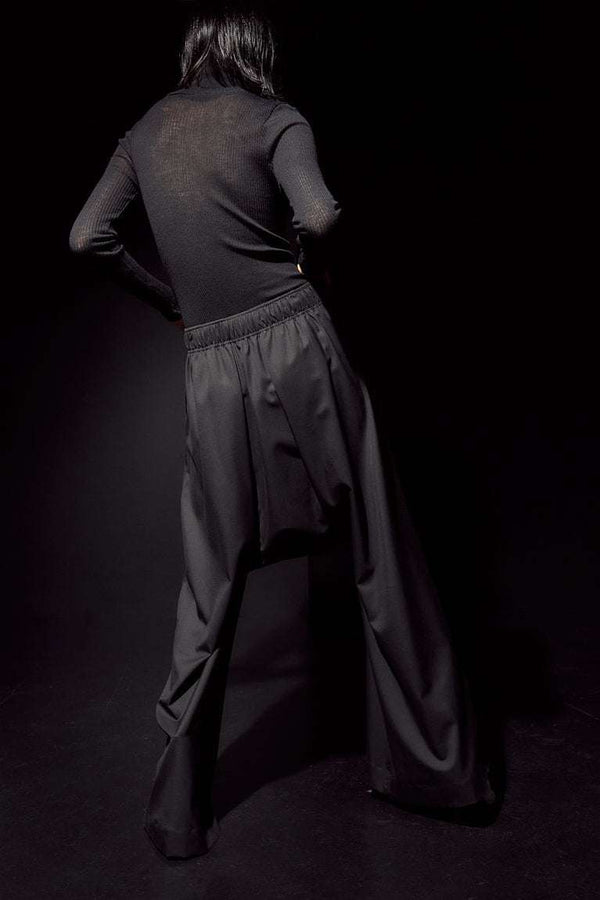 INTERNATIONAL CITIZEN.  Style: The Lanna Pant have a dropped crotch with excessive volume eased into an elastic waistband. Unisex Item. Female back body photo. Made of Italian Wool, certified (RWS) Responsible Wool Standard, Obsidian Black. Spiritually Infused, Sustainable Luxury Fashion in Berlin.
