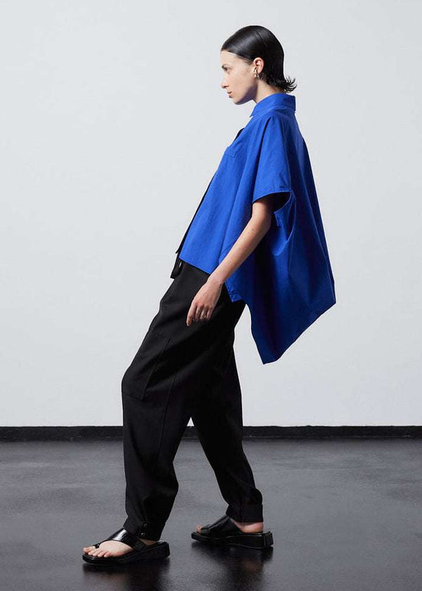 INTERNATIONAL CITIZEN.  Style: The Cubism Shirt is a 3-dimensional cube tilted on its axes to create a boxy minimal front body and dramatic drape in the back body. Unisex Item. Full body side view. Made of Italian Organic Cotton, Lapis Lazuli Blue. Spiritually Infused, Sustainable Luxury Fashion in Berlin.