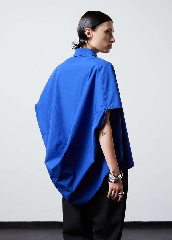 INTERNATIONAL CITIZEN.  Style: The Cubism Shirt is a 3-dimensional cube tilted on its axes to create a dramatic drape in the back body. Unisex Item. Cropped side back body. Made of Italian Organic Cotton, Lapis Lazuli Blue. Spiritually Infused, Sustainable Luxury Fashion in Berlin.