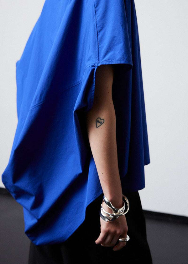 INTERNATIONAL CITIZEN.  Style: The Cubism Shirt is a 3-dimensional cube tilted on its axes to create a boxy minimal front body and dramatic drape in the back body. Unisex Item. Close up side view. Made of Italian Organic Cotton, Lapis Lazuli Blue. Spiritually Infused, Sustainable Luxury Fashion in Berlin.