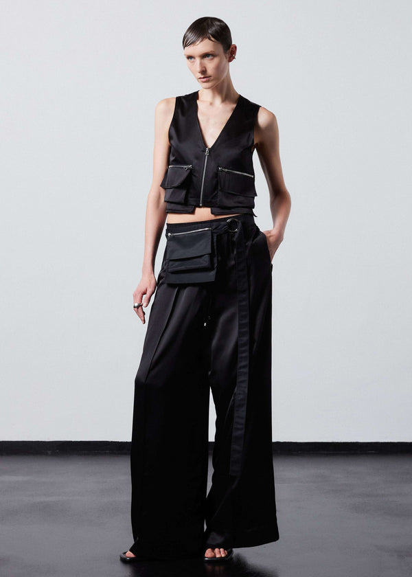 INTERNATIONAL CITIZEN.  Style: The Arcana Pant. Front full body view with x-body bag. Style has a relaxed fit with front pin-tucks and excessive volume eased into the waistband. Unisex Item. The pants are made of Italian organic silk in Obsidian Black. Spiritually Infused, Sustainable Luxury Fashion in Berlin.