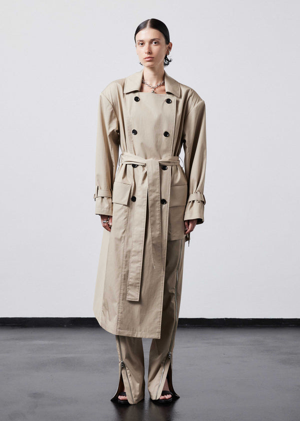 INTERNATIONAL CITIZEN.  Style: The Eclipse Jacket. A unisex, asymmetrical along the hemline and oversized with soft shoulder pads for collapsed structure. It is half lined, belted, double breasted, has extra-large pockets, and adjustable sleeve straps with silver rings. Front view worn closed. Made of Italian Organic Cotton, Dune. Spiritually Infused, Sustainable Luxury Fashion in Berlin.