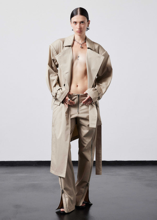 INTERNATIONAL CITIZEN.  Style: The Eclipse Jacket. A unisex, asymmetrical along the hemline and oversized with soft shoulder pads for collapsed structure. It is half lined, belted, double breasted, has extra-large pockets, and adjustable sleeve straps with silver rings. Front view worn open. Made of Italian Organic Cotton, Dune. Spiritually Infused, Sustainable Luxury Fashion in Berlin.