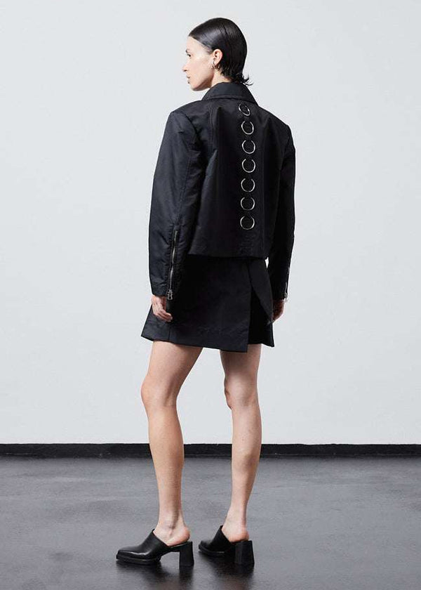 INTERNATIONAL CITIZEN.  Style: Ajna Jacket. Back full body view of a black boxy jacket with sporty tailoring, featuring square shoulders, tapered sleeves, and zipper closures. The jacket features 7-rings down the back body. The jacket is made from of Italian water repellent, post-consumer recycled Nylon Gaberdine. Spiritually Infused, Sustainable Luxury Fashion in Berlin.