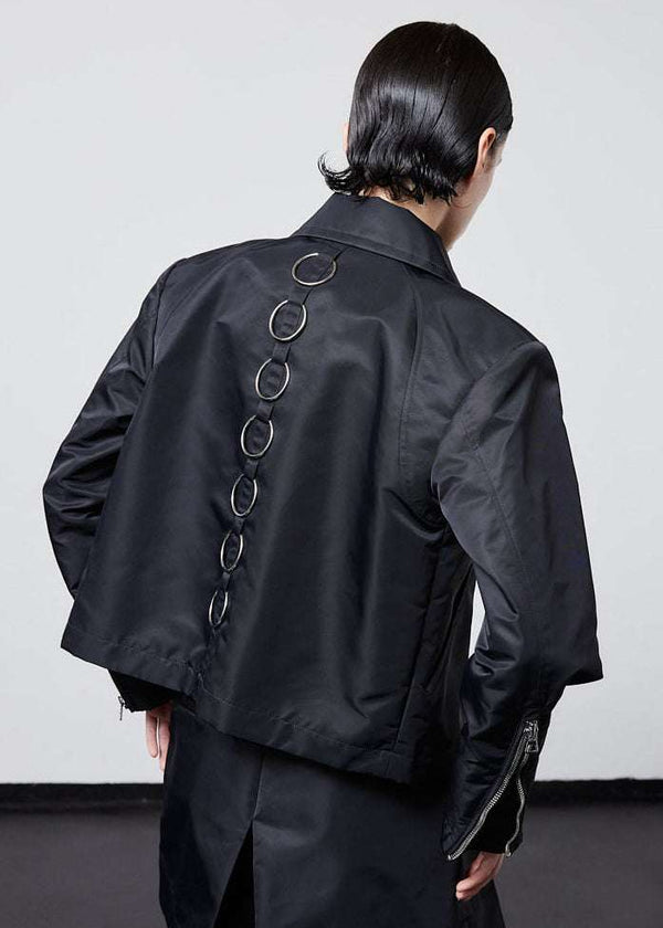 INTERNATIONAL CITIZEN.  Style: Ajna Jacket. Back view of a black boxy jacket with sporty tailoring, featuring square shoulders, tapered sleeves, and zipper closures. The jacket has 7-rings down the back body. The jacket is made from of Italian water repellent, post-consumer recycled Nylon Gaberdine. Spiritually Infused, Sustainable Luxury Fashion in Berlin.
