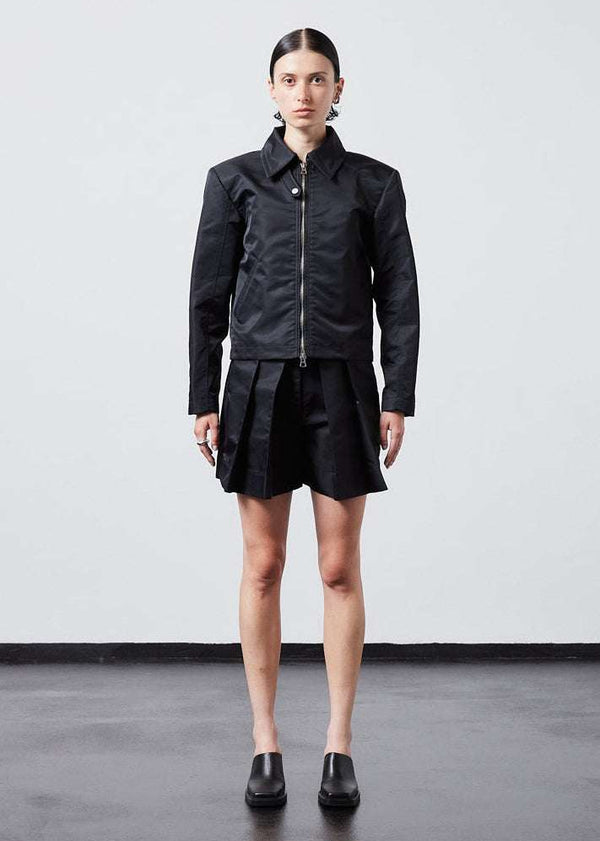 INTERNATIONAL CITIZEN.  Style: Ajna Jacket. A black boxy jacket with sporty tailoring, featuring square shoulders, tapered sleeves, and zipper closures. The jacket has a snap tab at the collar neckline & 7-rings down the back body. The jacket is made from of Italian water repellent, post-consumer recycled Nylon Gaberdine.  Fully body view. Spiritually Infused, Sustainable Luxury Fashion in Berlin.