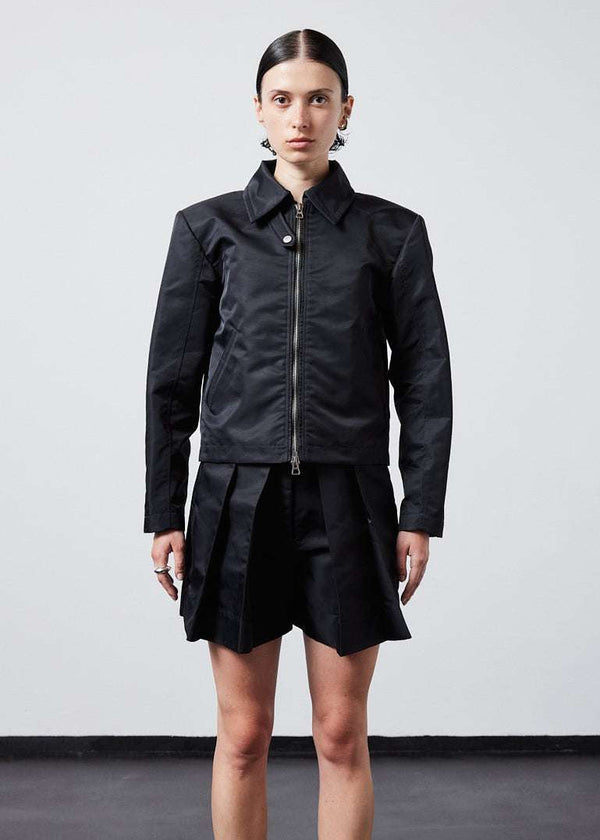 INTERNATIONAL CITIZEN.  Style: Ajna Jacket. A black boxy jacket with sporty tailoring, featuring square shoulders, tapered sleeves, and zipper closures. The jacket has a snap tab at the collar neckline. The jacket is made from of Italian water repellent, post-consumer recycled Nylon Gaberdine. Spiritually Infused, Sustainable Luxury Fashion in Berlin.