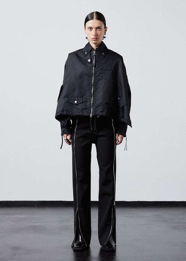 INTERNATIONAL CITIZEN.  Style: The Cube Coat, is a 3D cube tilted on its axes to create a boxy minimal front body and dramatic drape in the back body. It has zipper closures, and a drawcord at the front hemline and a utility pen pocket on the chest. Front full body view. Unisex style. Made of Italian post-consumer recycled Nylon, Obsidian Black. Spiritually Infused, Sustainable Luxury Fashion in Berlin.