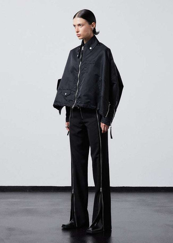 INTERNATIONAL CITIZEN.  Style: The Cube Coat, is a 3D cube tilted on its axes to create a boxy minimal front body and dramatic drape in the back body. Side front view. Unisex style. Made of Italian post-consumer recycled Nylon, Obsidian Black. Spiritually Infused, Sustainable Luxury Fashion in Berlin.