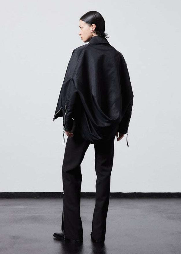 INTERNATIONAL CITIZEN.  Style: The Cube Coat, is a 3D cube tilted on its axes to create a boxy minimal front body and dramatic drape in the back body. Full body side back view. Unisex style. Made of Italian post-consumer recycled Nylon, Obsidian Black. Spiritually Infused, Sustainable Luxury Fashion in Berlin.