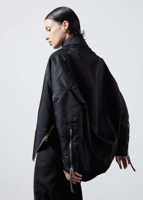 INTERNATIONAL CITIZEN.  Style: The Cube Coat, is a 3D cube tilted on its axes to create a boxy minimal front body and dramatic drape in the back body. It has zipper closures. Side back view. Unisex style. Made of Italian post-consumer recycled Nylon, Obsidian Black. Spiritually Infused, Sustainable Luxury Fashion in Berlin.