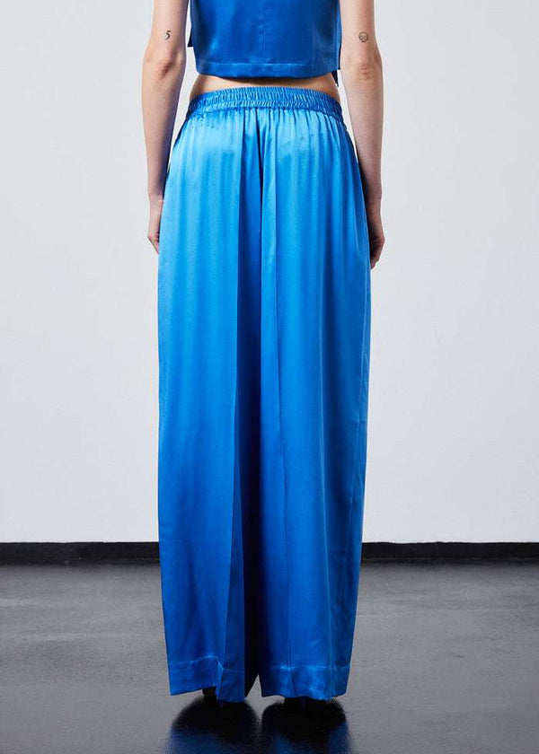INTERNATIONAL CITIZEN.  Style: The Arcana Pant. Back view has a relaxed fit with front pin-tucks and excessive volume eased into the waistband. Unisex Item. The pants are made of Italian organic silk in Azurite Blue. Spiritually Infused, Sustainable Luxury Fashion in Berlin.