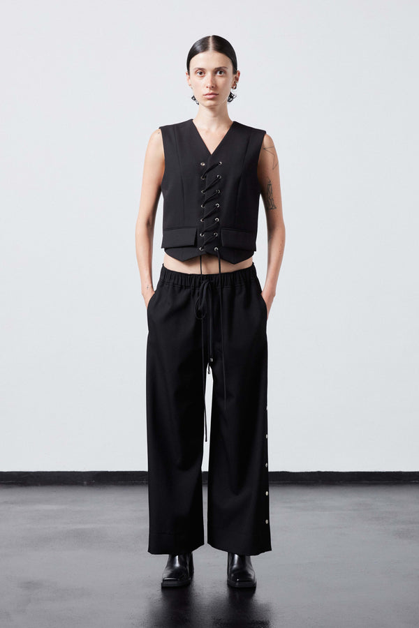 INTERNATIONAL CITIZEN.  Style: The Track Trouser has a smooth back waistband and elastic front with a drawcord tunnel at the front. Silver metal snaps down the side and cropped ankle length. Unisex item. Made of Italian Wool RWS, Obsidian Black. Spiritually Infused, Sustainable Luxury Fashion in Berlin. Full front photo.