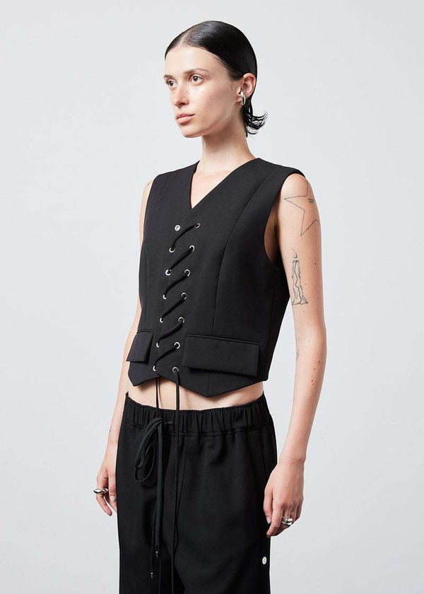 INTERNATIONAL CITIZEN.  Style: The Stitch Vest features a high neckline with overlapping front closure held with an eyelet stitch lacing detail. Made of Italian Wool RWS, Obsidian Black. Spiritually Infused, Sustainable Luxury Fashion in Berlin. Side front photo.