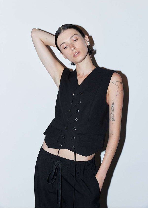 INTERNATIONAL CITIZEN.  Style: The Stitch Vest features a high neckline with overlapping front closure held with an eyelet stitch lacing detail. Made of Italian Wool RWS, Obsidian Black. Spiritually Infused, Sustainable Luxury Fashion in Berlin. Front photo.