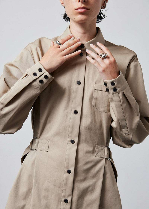 INTERNATIONAL CITIZEN.  Style: Artist Shirt Dress. Close up front view. Style has an oversized shirt with a pen pocket at the chest, open underarms for breathability, and back belt ties that adjust at the front with silver rings. The shirt are made of Italian organic Cotton Twill in Dune. Spiritually Infused, Sustainable Luxury Fashion in Berlin.