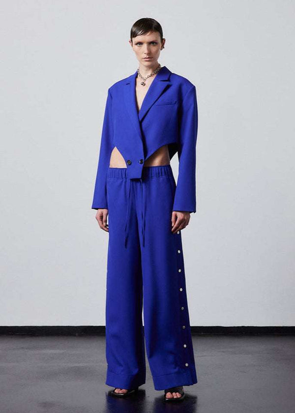 INTERNATIONAL CITIZEN.  Style: The Track Trouser has a smooth back waistband and elastic front with a drawcord tunnel at the front. Silver metal snaps down the side and cropped ankle length. Unisex item. Made of Italian Wool RWS, Lapis Lazuli Blue. Spiritually Infused, Sustainable Luxury Fashion in Berlin. Full front view.