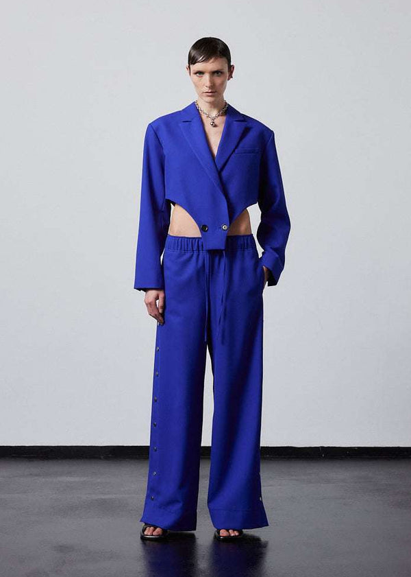 INTERNATIONAL CITIZEN.  Style: The Track Trouser . Blue cropped track trousers with button details and elastic waistband, part of the Track Trouser collection for women and men, stylish and comfortable for casual wear. Unisex item. Made of Italian Wool RWS, Lapis Lazuli Blue. Spiritually Infused, Sustainable Luxury Fashion in Berlin. Full front view.