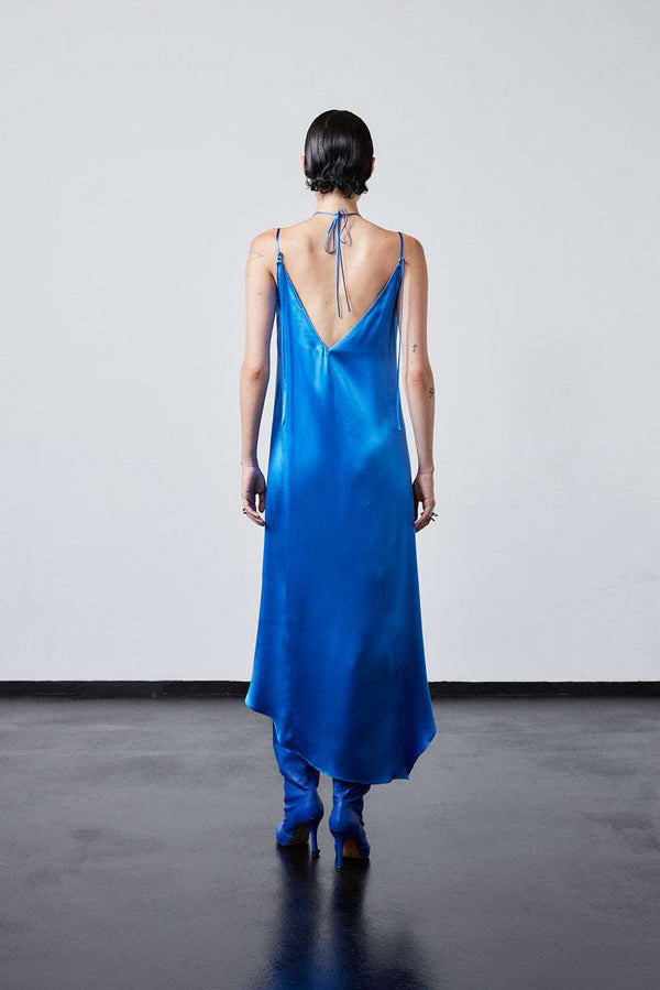 INTERNATIONAL CITIZEN.  Style: The Crystalline Dress. Model in blue satin dress with skiny strap ties. Made of Organic Silk, Azurite Blue. Spiritually Infused, Sustainable Luxury Fashion in Berlin.