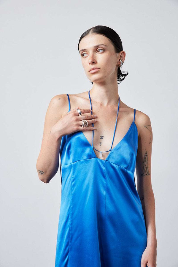 INTERNATIONAL CITIZEN.  Style: The Crystalline Dress. Front view of model in blue satin dress with layered hem and boots. Made of Organic Silk, Azurite Blue. Spiritually Infused, Sustainable Luxury Fashion in Berlin.
