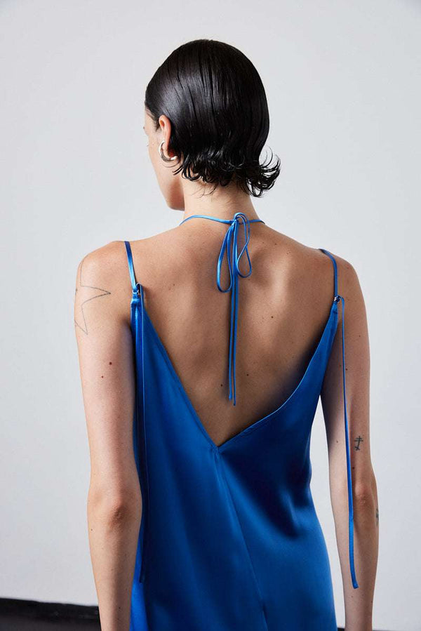 INTERNATIONAL CITIZEN.  Style: The Crystalline Dress. Back view of blue satin dress with tie straps and low V neckline. Made of Organic Silk, Azurite Blue. Spiritually Infused, Sustainable Luxury Fashion in Berlin.