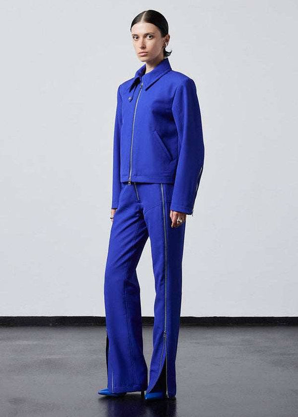 INTERNATIONAL CITIZEN.  Style: Ajna Jacket - a blue boxy jacket with sporty tailoring, featuring square shoulders, tapered sleeves, and zipper closures. The jacket is made from of Italian Wool in Lapis Lazuli Blue. Full body photo 3/4 turn. Spiritually Infused, Sustainable Luxury Fashion in Berlin.