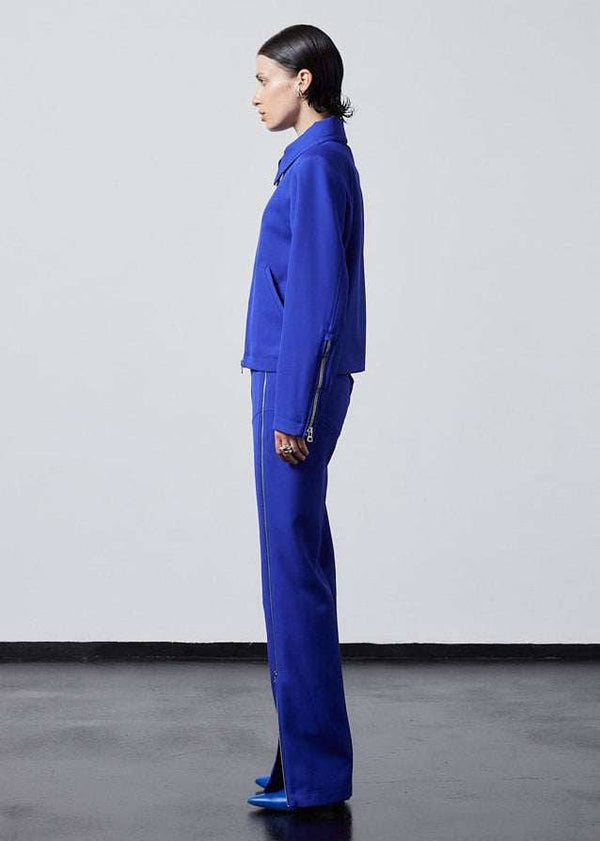INTERNATIONAL CITIZEN.  Style: Ajna Jacket - a blue boxy jacket with sporty tailoring, featuring square shoulders, tapered sleeves, and zipper closures. The jacket is made from of Italian Wool in Lapis Lazuli Blue. Full body side view. Spiritually Infused, Sustainable Luxury Fashion in Berlin.